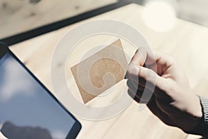 Closeup Man Showing Blank Craft Business Card, Holding Hand Modern Digital Tablet.Wood table Blurred Background.Mockup