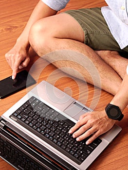 Closeup of a man sitting typing on keybord of his laptop and his smartphone simultaneously.