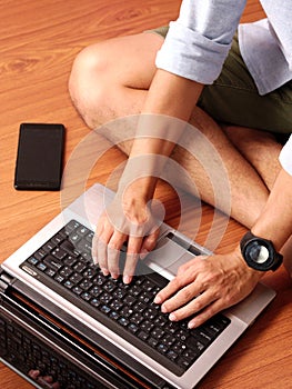 Closeup of a man sitting typing on laptop wearing smart-watch and mobilephone beside.