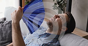 Closeup man suffers from heat wave blue fan cooling himself