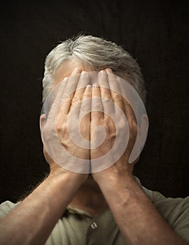 Closeup of a man trying to hide his feelings by covering his face with his hands