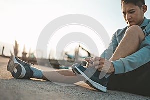 Closeup of man tying shoe laces on the road before running in sunset. Sport and workout concept