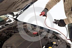 Closeup of man under bonnet with starter cables