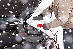 Closeup of man under bonnet with starter cables