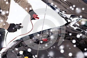 Closeup of man under bonnet with starter cables