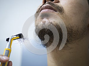 Closeup man use yellow shaver shaving messy beard and mustache on his face in bathroom