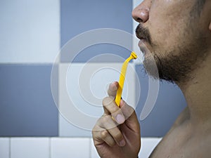 Closeup man use yellow shaver shaving messy beard and mustache on his face in bathroom