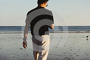 Closeup of a man walking in a black t-shirt towards the sea.