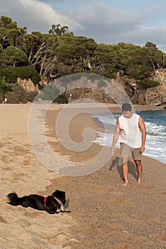 Closeup of a man  walking his dog along a sandy beach, with the waves of the ocean in the background