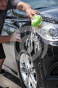 Closeup man washing new black car with big soft sponge, soap suds and bucket