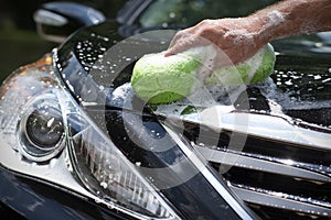 Closeup man washing new black car hood with big soft sponge, soap suds