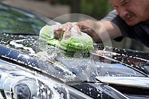 Closeup man washing new black car hood with big soft sponge, soap suds and bucket