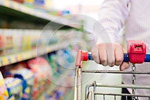 Closeup on man or woman hand in shop with shopping trolley or cart on the supermarket shelf background