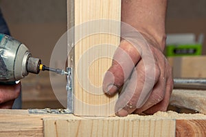 Closeup man works with handheld battery screwdriver on wooden surface