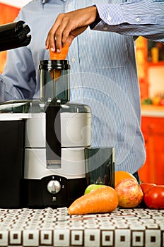 Closeup man's hands using juice maker, inserting carrot into machine, healthy lifestyle concept