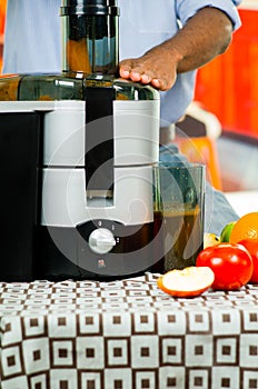 Closeup man's hands using juice maker, inserting carrot into machine with orange liquid bowl connected, healthy