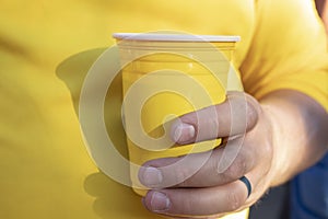 Closeup of man in yellow shirt wth working man`s hands and nails and black wedding ring holding yellow plastic drinking cup - sel