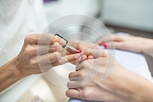 Closeup of manicurist applying shiny red nail polish