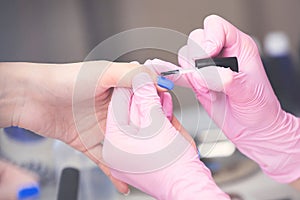 Closeup of manicurist in pink rubber gloves applying blue nail polish on female nails