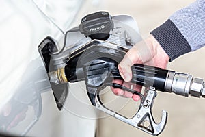 Closeup of mans hand pumping gasoline fuel in car at gas station.