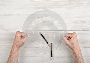Closeup masculine fists clenched on wooden panel with broken pen