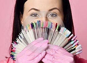 Closeup. Master in pink medicine gloves keeps with nail varnish samples display on background