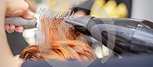 Closeup of master& x27;s hand with blow-drying and hairbrush blowing female red hair in a salon.