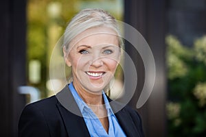 Closeup Of A Mature Businesswoman Smiling At The Camera. In front of her office