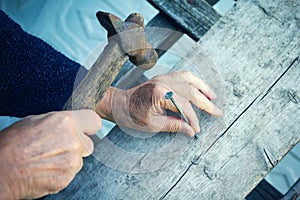 Closeup of mature man hands nails with old hammer