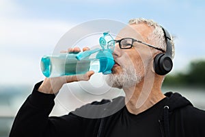 Closeup of mature sportsman drinking water during workout outdoors