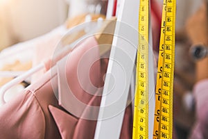 Closeup of measuring tape and line of fashion pastel pink colored woman shirts with wooden hangers in clothing shop