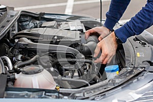 Closeup of mechanic hands checking motor under the hood in the broken car. Repairing of the vehicle concept. Automobile service.