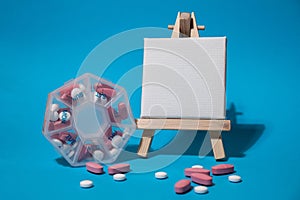 Closeup of medical pill box with doses of tablets for daily take medicine with white pink drugs and capsules with paper