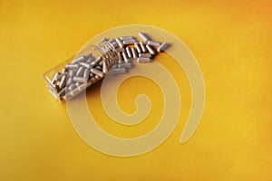 Closeup of medical pills spilling out of a bottle isolated on a yellow background