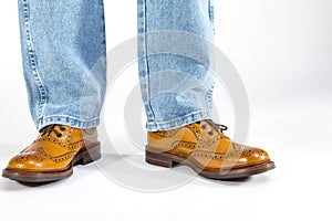 Closeup of Mens Legs on Brown Oxford Brogue Shoes. Posing in Blue Jeans Against White Background