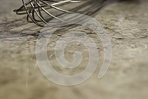 Closeup of metal wisk on marbled kitchen counter, background wit