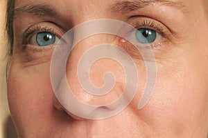 Closeup of middle aged woman face with blue eyes. Real skin without make up and correction. Look at camera.  Smiled