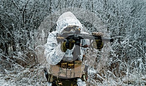 Closeup military man in white camouflage uniform with hood and aims of the machinegun. Horizontal photo side view photo