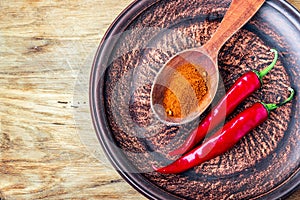 Closeup milled chili peppers flakes and chili powder on dark plate, fresh red ripe hot chili on old wood board background with cop