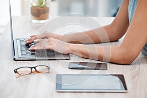 Closeup of mixed race business womans hands and fingers typing on laptop keyboard at a table in an office. One female