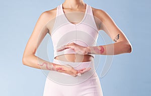 Closeup mixed race fitness woman gesturing around her tummy in studio against a blue background. Young hispanic female