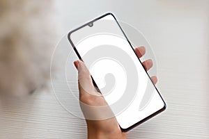 Closeup mockup image of a woman`s hand holding mobile phone with blank white screen in a cozy space