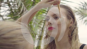 Closeup of model receiving makeup during photo shoot, makeup artist adjusting blush on her face