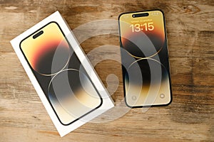Closeup modern gadget apple on wooden table, unpacks, testing new gold smartphone iPhone 14 Pro Max with Super Retina display,