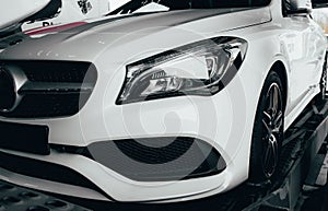 Closeup modern luxury white front lights headlight and head lamp rims of powerful sport car. Dealership office showroom sale hype