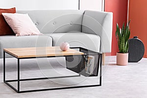 Closeup of modern wooden and metal coffee table next to stylish grey couch in trendy living room