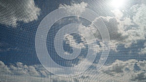 Closeup of mosquito wire screen with sun ray on blue sky and white clouds in background