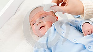 Closeup of mother cleaning face and eyes of her newborn baby son with cooton pad. Concept of babies and newborn hygiene