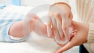 Closeup of mother cleaning newborn baby body and applying moisturizing baby oil with cotton pad