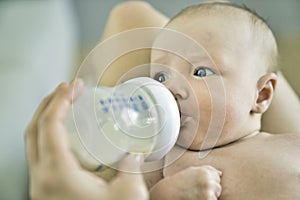 Closeup of a mother feeding baby with milk bottle at home